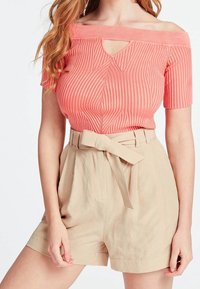 Korallfarbenes, geripptes Off-Shoulder-Top mit einer Schlüsselloch-Detail, kombiniert mit hoch geschnittenen beigen Shorts mit einem gebundenen Gürtel und dezenten vertikalen Streifen.