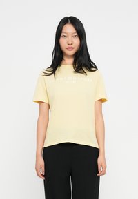 Żółta bawełniana koszulka z krótkim rękawem, okrągłym dekoltem i białym logo z napisem "TOMMY HILFIGER EST. 1985" wydrukowanym z przodu.