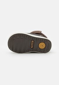 Brun teksturert sneakersåle med en hvit gummikant, med et sirkulært logo og markerte mønstre for godt grep.