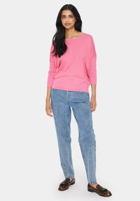 Fuksijas adīta džemperis ar trim ceturtdaļu piedurknēm, kombinēts ar gaiši ziliem taisnās kājas džinsiem un brūnām mokasīnām. Gluda tekstūra, brīvs piegriezums.