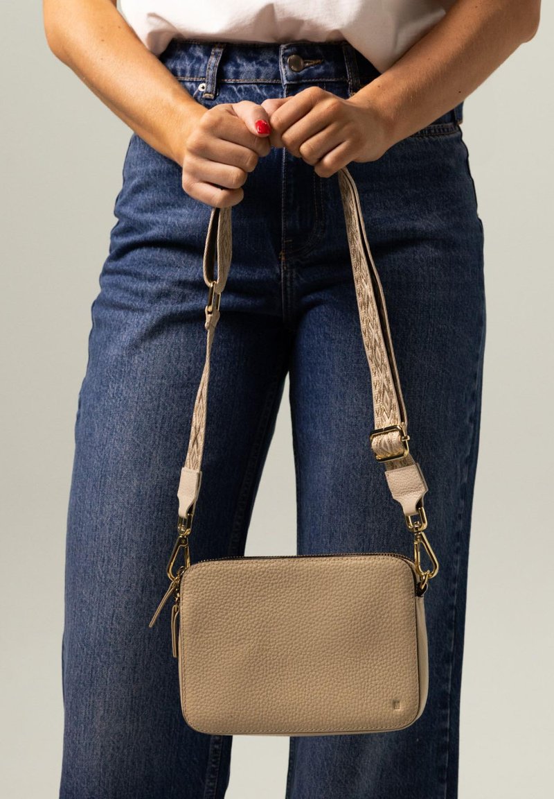 Beige Leder Umhängetasche mit strukturiertem Finish, goldenen Hardware-Elementen und gewebtem Trageriemen. Kompakte rechteckige Form, Reißverschlussverschluss, minimalistisches Design.