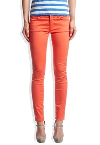 Pomarańczowe dopasowane dżinsy o gładkiej fakturze i pięciu kieszeniach, z zapięciem na zamek błyskawiczny i szlufkami na pasek, zestawione z niebieską i białą koszulą w paski.
