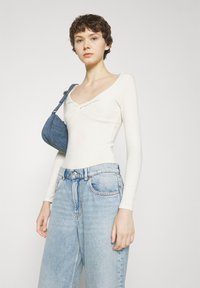 Body bianco a maniche lunghe con scollatura a giro, abbinato a jeans high-waisted blu chiaro. Modella porta una piccola borsa in tessuto blu.