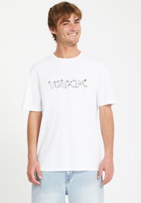 T-shirt en coton blanc avec un logo "VOLCOM" stylisé en noir sur le devant. Manches courtes et coupe décontractée avec un col rond.