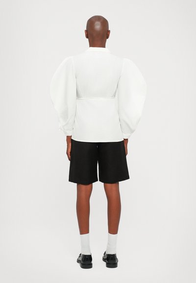 Witte blouse met pofmouwen en een getailleerde taille, gecombineerd met zwarte shorts. Gladde textuur met een schoon, minimalistisch ontwerp.