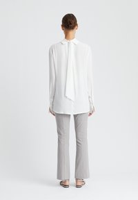 Witte blouse met lange mouwen en een strikdetail op de rug, gecombineerd met lichtgrijze flared broek, met een zachte textuur en een getailleerde pasvorm.