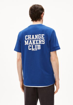 Blauwe katoenen T-shirt met "CHANGE MAKERS CLUB" in witte blokletters op de achterkant. Korte mouwen, ronde hals en een relaxte pasvorm.