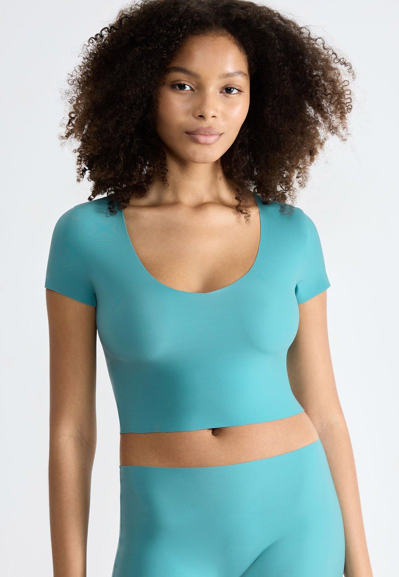 Turkusowy crop top sportowy z okrągłym dekoltem i krótkimi rękawami. Gładka tekstura, dopasowany krój, zestawiony z pasującymi spodniami o wysokim stanie.
