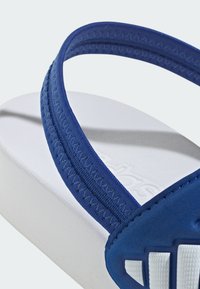 Modra japonka z teksturiranim trakom iz blaga, belim gumijastim podplatom in detajli z logotipom. Trak ima cikcak šive za dodatno podrobnost.