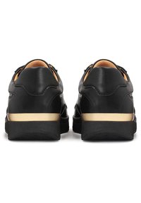 Baskets en cuir noir vues de dos avec un col rembourré beige et une bande dorée au-dessus de la semelle noire.