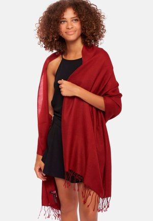 Châle rouge en matériau léger, doté d'une texture douce et d'un bord frangé, drapé sur les épaules, complétant une tenue noire.