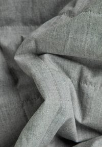 Strukturiertes graues Gewebe mit einem subtilen Geflecht, das sichtbare Nähte entlang der Kanten und sanfte Falten aufweist und ein lässiges Design betont.