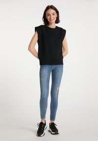 Fekete ujjatlan pulóver kerek nyakkal, bordázott aljú, világoskék skinny farmernadrággal és fekete sportcipővel párosítva.