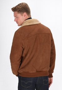 Brun ruskindsjakke med en fuzzy beige krave, der har en afslappet pasform, ribbede manchetter og en glat overfladestruktur.