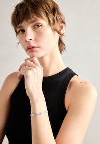 Silver bracelet with multiple rows of small gemstones, worn on a hand resting under the chin, against a neutral background.