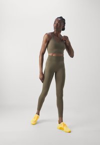Un top sporty court en vert olive et un legging taille haute en tissu extensible ; assortis à des chaussures de sport jaunes éclatantes.