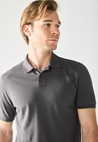 Gray polo shirt with a collar, short sleeves, and a three-button placket. Made of smooth fabric with a subtle texture.