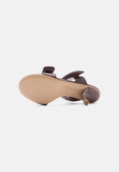 Καφέ δερμάτινο σανδάλι με τακούνι, φαίνεται από τη σόλα, με μυτερό τακούνι και ρυθμιζόμενο λουρί στον αστράγαλο σε λευκό φόντο.