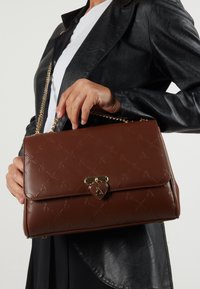 Brown leather handbag with embossed pattern, gold heart-shaped clasp, and a chain strap. The bag has a structured design and smooth texture.