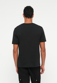 Tricou negru din bumbac, cu mâneci scurte și decolteu rotund, având un design simplu și o tivă dreaptă la talie.