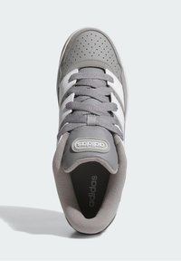 Sivá atletická obuv s perforovaným vrchom, bielymi pruhmi a sivými šnúrkami. Má textúrovanú podrážku a okrúhly logo na jazyku.