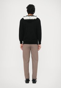 Fekete kötött kapucnis pulóver csíkos szürke gallérral, bézs szabott nadrággal és fekete cipővel párosítva; hátulnézetből.