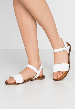 Weiße Ledersandalen mit geflochtenem Riemen-Design, verstellbarem Knöchelriemen und flacher brauner Sohle, die minimalistischen Stil und Komfort zeigen.