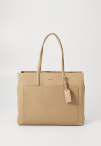 Sac fourre-tout en cuir camel avec deux bretelles, texture lisse, une poche avant et un petit détail de porte-étiquette. Design minimaliste.