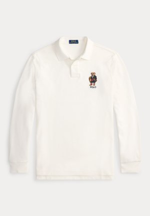 Camisa polo de manga larga blanca en punto de algodón con cuello. Presenta un oso bordado con traje en el lado izquierdo del pecho junto con el texto "POLO".