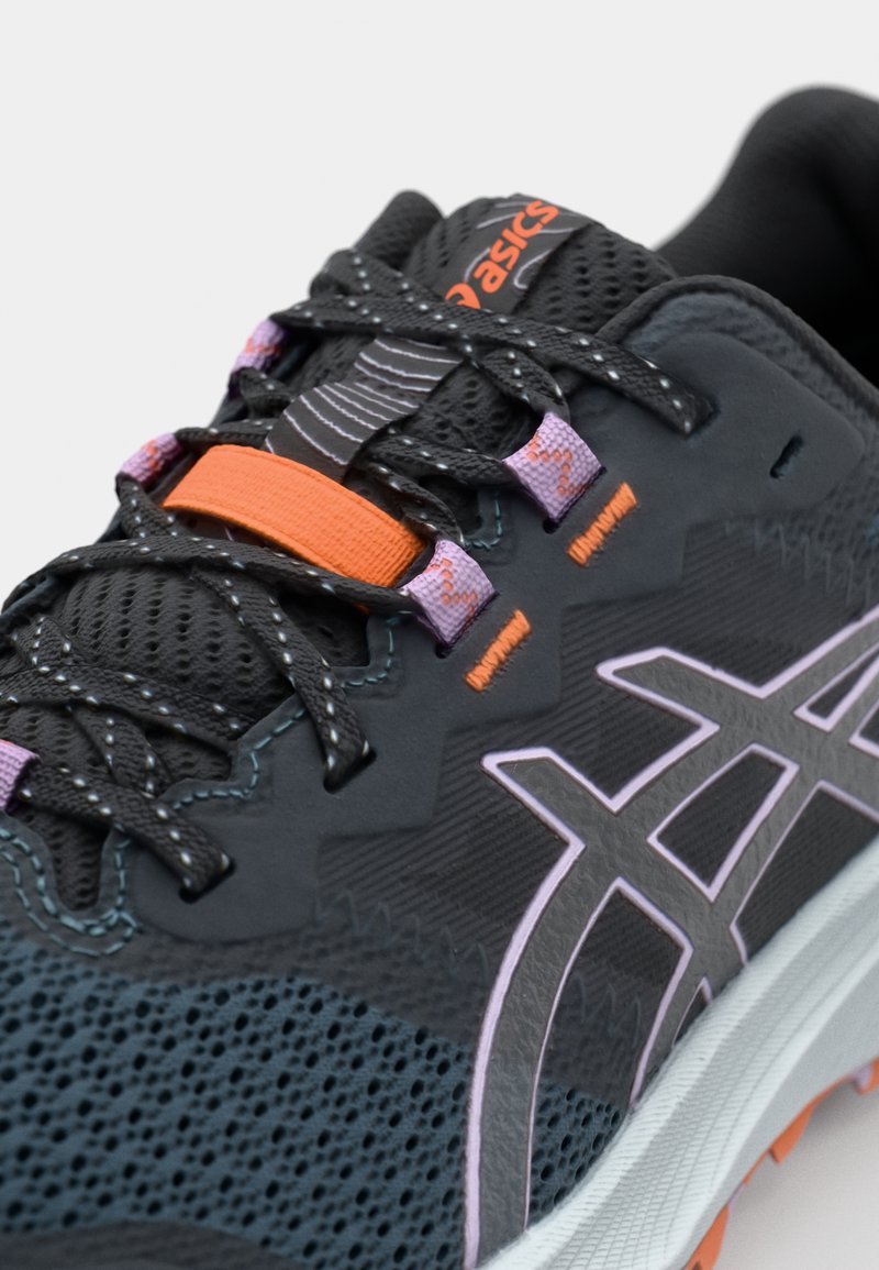 Zapatilla de running con parte superior de malla negra, detalles en laces morados y un toggle naranja. Presenta una entresuela gris claro y una suela texturizada.