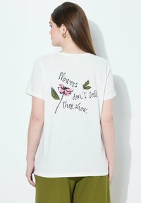 Camiseta blanca de algodón con un diseño floral y texto impreso en la parte trasera. La camiseta tiene mangas cortas y un corte holgado.