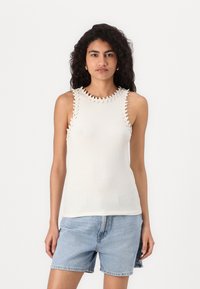 Top sin mangas blanco acanalado con un borde decorativo en forma de concha en los hombros, combinado con pantalones cortos de mezclilla azul claro. Diseño minimalista y forma ajustada.