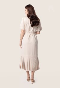 Robe midi beige plissée à manches courtes, dotée d'une ceinture nouée à la taille. Tissu lisse, éclat subtil et silhouette fluide.