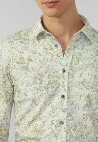 Hemd in Hellblau mit einem strukturierten Blumenmuster in Beige und Grün. Verfügt über einen Kragen und fünf Knöpfe auf der Vorderseite.