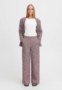 Zweiteiliges Outfit mit einem strukturierten, lila-weißen gemusterten Cardigan und dazu passenden weiten Hosen, kombiniert mit einem weißen Oberteil.