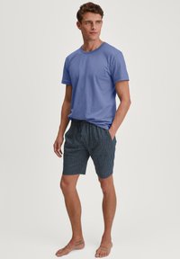 Blauw katoenen t-shirt gecombineerd met marineblauwe shorts met een wit geometrisch patroon. De shorts hebben een elastische tailleband en zijzakken.