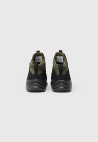 Black and olive green sneakers with a high-top design, textured fabric upper, and thick, wavy rubber sole. Features rear pull tabs.