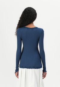 Haut à manches longues en maille côtelée marine avec un col en dentelle festonné et des poignets, design ajusté et texture douce, associé à une jupe blanche fluide.