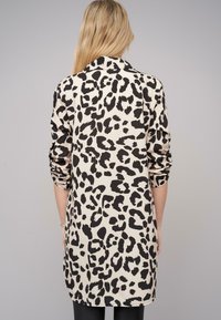 Langarmhemd mit Leopardenmuster in Beige und Schwarz. Glattes Material, mit Kragen, aufgerollte Ärmel und abgerundeter Saum.