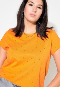 Orange t-shirt tillverkad av mjukt material, med rund halsringning och korta ärmar, prydd med spridda små strass för detalj.