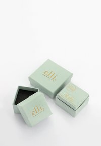 Mintgrønne papirgaveæsker stablet, med gyldent teksttryk. En æske er sekskantet med sort inderside, de andre er rektangulære med etiketter.