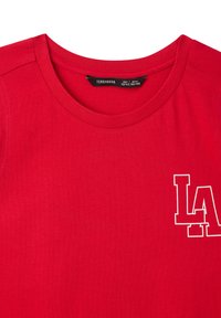 T-shirt in cotone rosso con scollatura rotonda e grafica bianca "LA" sul lato sinistro. Tessuto liscio con maniche corte.