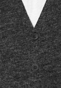 Närbild av en mörkgrå ullkofta med två svarta knappar och en vit skjorta synlig under.