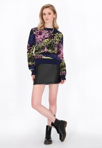 Maglione lavorato a maglia con un motivo colorato in rosa, giallo e blu, abbinato a una mini gonna nera e a stivaletti neri con lacci.