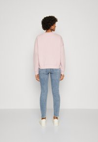 Sudadera rosa claro con cuello redondo y hombros caídos, combinada con jeans skinny azul claro y zapatillas blancas, vista desde atrás.