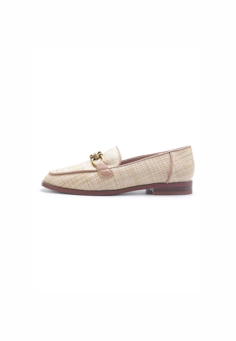 Mocasines beige hechos de material texturizado con una suela plana marrón. Presenta una tira de cuero marrón claro con un acento metálico. Se muestra vista lateral.