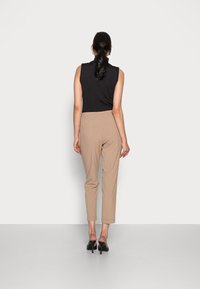 Svart ärmlös topp, beige tapered byxor med elastisk midja och svarta högklackade skor. Enkelt design, slät textur, inga mönster synliga.