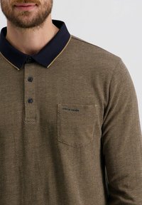Langarm polo shirt in bruin met een visgraatpatroon, voorzien van een marineblauwe kraag, drie knopen en een borstzak met branding.