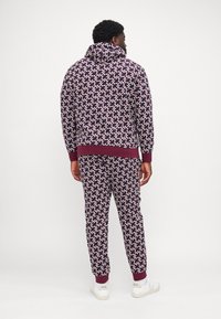 Mørkerød mønstret træningsdragt bestående af en pullover med hætte og tætsiddende bukser, fremstillet af blødt materiale, med ribbet mansjetter og kant.