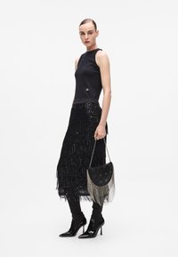 Black sleeveless top with a metallic accent, paired with a black fringed sequin skirt. The model holds a black handbag with silver fringe.